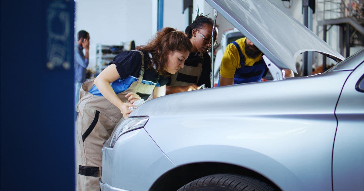 Team of mechanics in car service using inspection lamp to fix automobile in need of repairments. Colleagues service broken vehicle, checking for faulty engine using professional tools, dolly out shot
