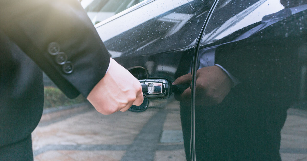 Hand of businessman opening door of car with key.